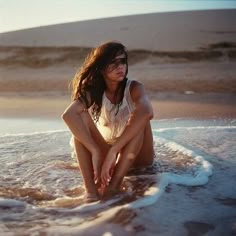 a woman is sitting in the water at the beach and she has her hands on her knees