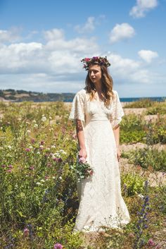 a woman standing in a field with flowers on her head and wearing a white dress