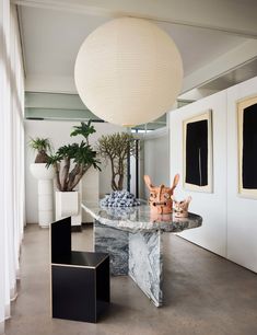 a marble table surrounded by black and white chairs in a room with potted plants