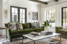 a living room filled with green couches and pillows on top of a rug in front of two windows