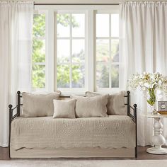 a day bed sitting in front of a window next to a vase with flowers on it