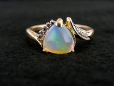 "Polished to perfection and filled with glitters of light in every shade of the rainbow, this gorgeous opal gemstone shines with fire from each of its three facets. We love the nearly heart shaped profile of this trillion cut stone, and the slightly asymetrical flow it gives the gold and diamond setting! Metal: 14K Yellow Gold Gem: Opal 1.53 Carats Gem Measurements: 8.6 mm, Trillion Cut Accents: 8 Diamonds totaling .10 Carat Ring Size: 11 Marks: \"14K\" Stamped on the inside band SKU #: VW4YPF-N Opal Ring With Diamond Accents For Gift, Gift Opal Ring With Diamond Accents, Multicolor Opal Jewelry For Anniversary, Iridescent Opal Jewelry For Anniversary, Yellow Gold Opal Ring With Diamond Accents For Gift, Elegant Opal Heart Cut Jewelry, Opal Jewelry With Diamond Accents As A Gift, Elegant Heart Cut Opal Jewelry, Elegant Iridescent Opal Ring For Anniversary