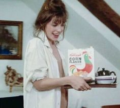 a woman holding a box of cereal on top of a wooden shelf in a living room