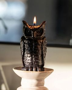 an owl figurine sitting on top of a white pedestal with a lit candle