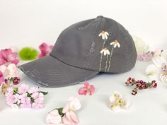 a baseball cap with daisies on it surrounded by pink and white flowers, all in front of a white background