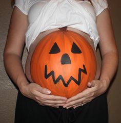 a pregnant woman holding a carved pumpkin in her hands, with the belly painted like a jack - o'- lantern