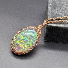 a gold necklace with an opal stone in the center on a black surface next to a box