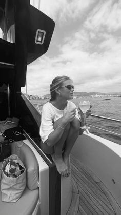 a woman sitting on the back of a boat looking out at the water and holding a drink