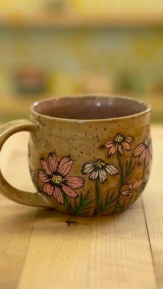 a coffee cup sitting on top of a wooden table with flowers painted on the side