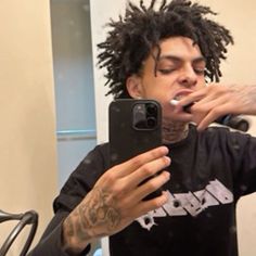 a man with dreadlocks taking a selfie in front of a mirror while brushing his teeth