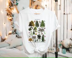 a white t - shirt with trees on it hanging from a hanger in front of a bed