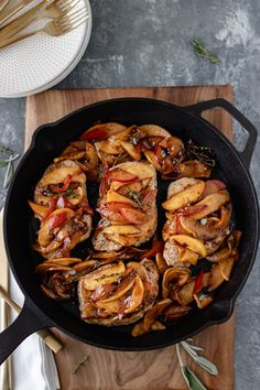 an iron skillet filled with meat and vegetables on top of a wooden cutting board