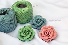 three crocheted roses sitting next to each other in front of yarn and knitting needles