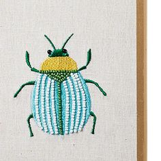 an embroidered beetle on a white canvas with green and yellow stripes, sitting in front of a wooden frame