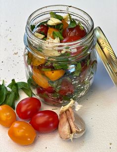 a jar filled with lots of different types of vegetables next to some garlic and tomatoes