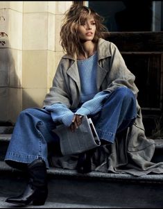 a woman is sitting on the steps with her hand in her pocket and looking off to the side