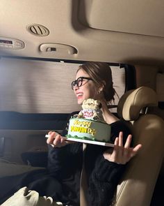 a woman sitting in the back seat of a car holding a cake