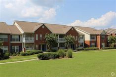 a row of brick apartment buildings with trees in the foreground and bushes on either side