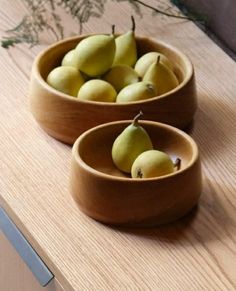 two wooden bowls filled with pears on top of a table