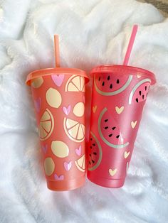 two plastic cups with straws and fruit on them sitting on a white furnishing