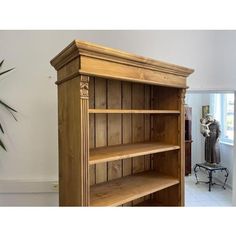 a wooden bookcase sitting in the corner of a living room next to a potted plant