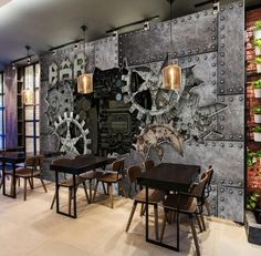 a restaurant with tables and chairs in front of a large metal wall mural that has gears on it