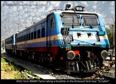 a blue and yellow train traveling down tracks next to power lines with clouds in the background