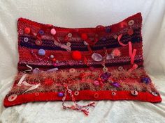 a red decorative pillow with buttons and ribbons on the bottom is sitting on a white sheet