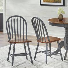 two wooden chairs sitting at a table with a vase on top of it in front of a white wall