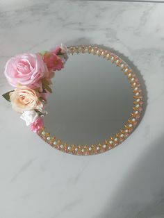 a round mirror with flowers on it sitting on a marble counter top next to a pink rose