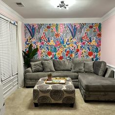 a living room with grey couches and a colorful wallpaper behind the sectional sofa