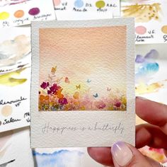 a person holding up a card with watercolors on it and the words happiness is beautiful