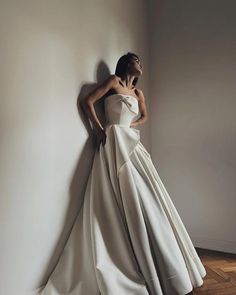 a woman in a white dress leaning against a wall