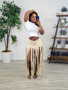 a woman taking a selfie while wearing a white crop top and fringed skirt