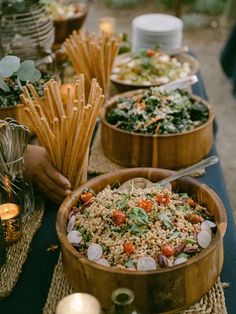 a table topped with wooden bowls filled with rice and veggies next to other foods