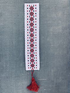 a cross stitch bookmark with a red tassel hanging from it's side