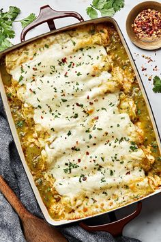 a casserole dish with cheese and herbs on the side next to a wooden spoon