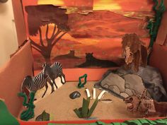 an open cardboard box with fake animals and plants in the inside, including two zebras