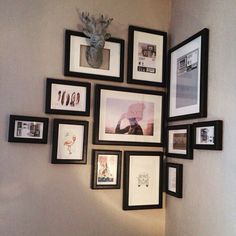 a wall filled with lots of framed pictures next to a vase on top of a table