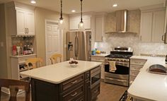 a large kitchen with an island, stove and refrigerator in the center is decorated with hanging lights