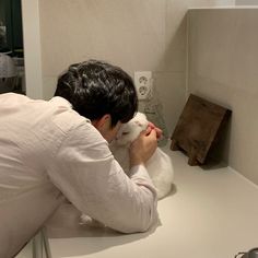 a man holding a white stuffed animal in his hands while sitting on a counter top