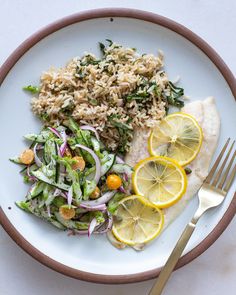 a white plate topped with fish and rice next to lemon wedges, as well as a salad