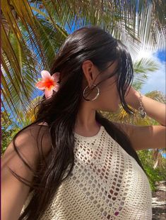 a woman with long hair wearing large hoop earrings and a flower in her hair, standing on the beach