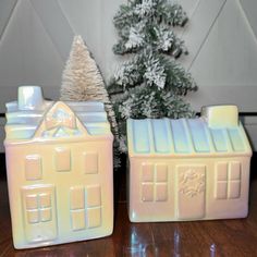 two ceramic houses sitting on top of a wooden table next to a small christmas tree