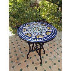 a blue and white mosaic table sitting on top of a tiled floor next to trees