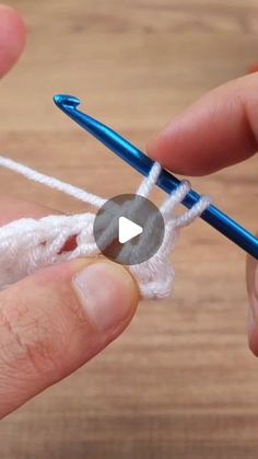 someone crocheting the end of a piece of white yarn with a blue needle