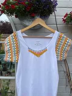 a white top with crochet on it hanging from a wooden hanger next to flowers