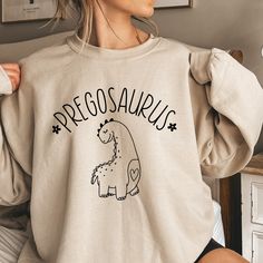 a woman wearing a sweatshirt that says prego saukus with a dinosaur drawn on it