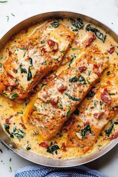 two pieces of fish covered in cheese and spinach on top of a skillet