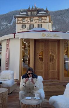 a woman sitting on a chair in front of a building with snow covered mountains behind her